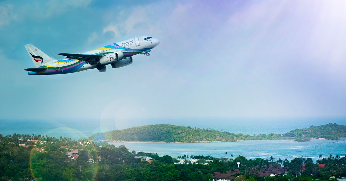 Airplane soaring over Koh Samui island, Thailand, showcasing a vibrant tropical landscape in daylight.