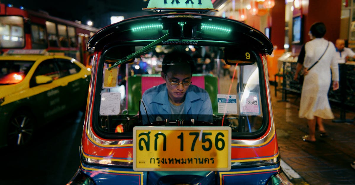 Tuk-tuk taxi driver focused while navigating through Bangkok's lively city streets at night.
