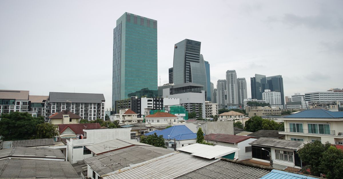 Urban skyline featuring towering skyscrapers above residential rooftops under a cloudy sky.