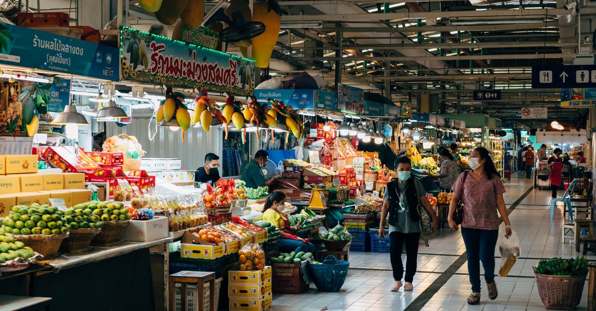 Asian indoor market with fruit stalls and shoppers wearing masks, showcasing vibrant produce.