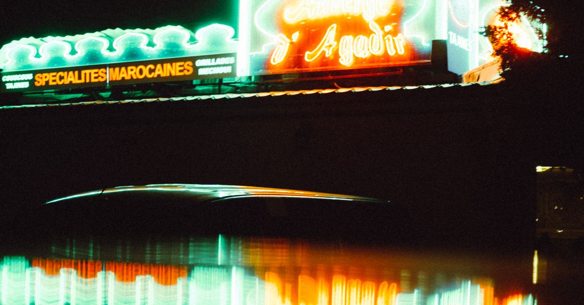 Colorful neon signs illuminate a night scene, reflecting vividly in water. A moody and urban atmosphere captured.