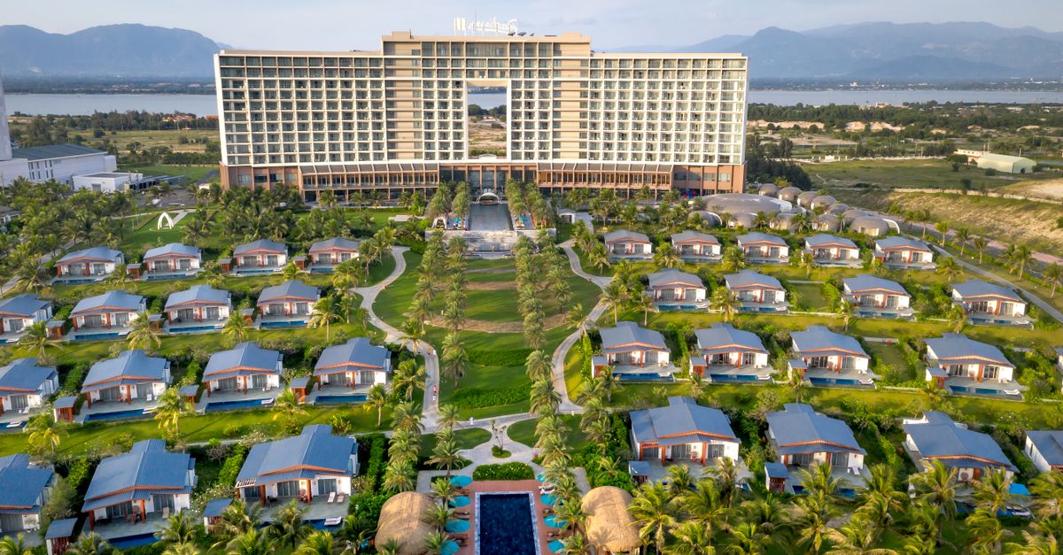 Aerial view of a luxury resort with bungalows surrounded by mountains and palm trees.