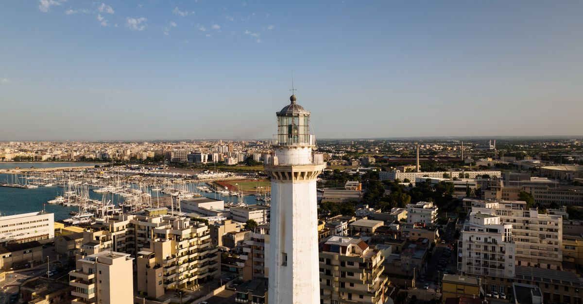 A stunning drone shot of a lighthouse in an urban coastal cityscape under a clear blue sky.
