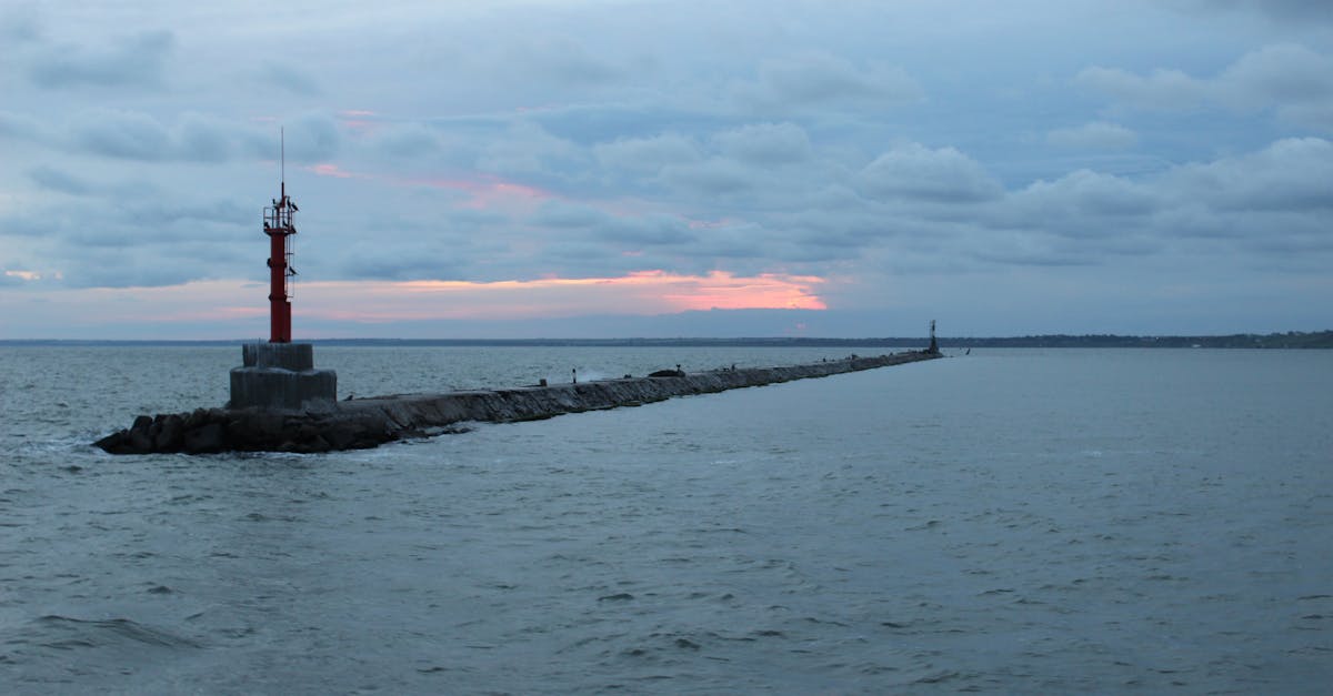 A tranquil scene of a lighthouse on a breakwater amid a vast sea at sunset.