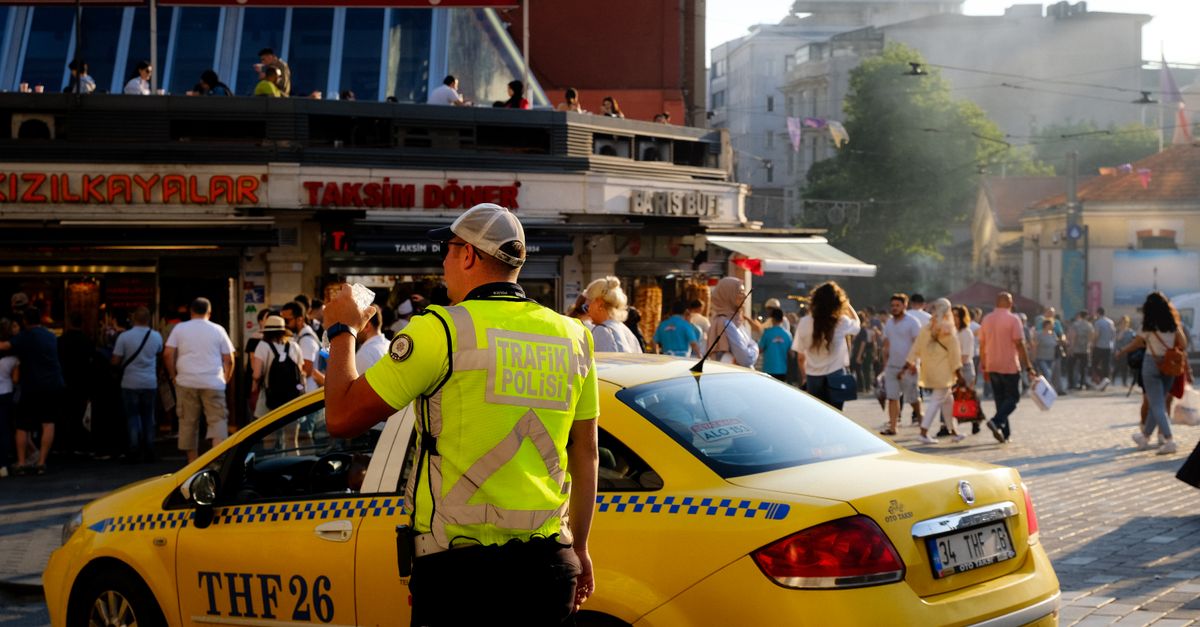 Traffic officer directs vehicles near a busy street in Istanbul with a yellow cab and pedestrians.