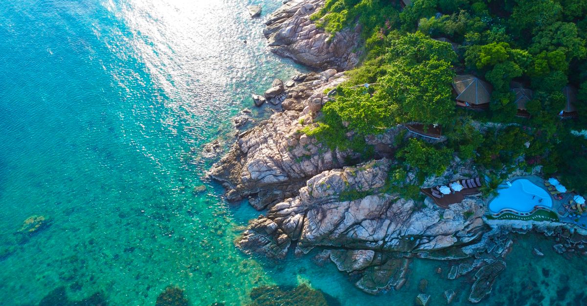 Drone view of tropical shoreline with clear turquoise waters and lush greenery.