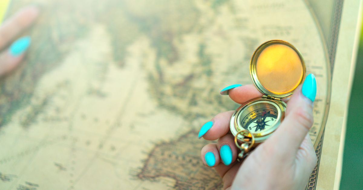 Close-up of a hand holding a vintage compass over an ancient map, symbolizing exploration and travel.