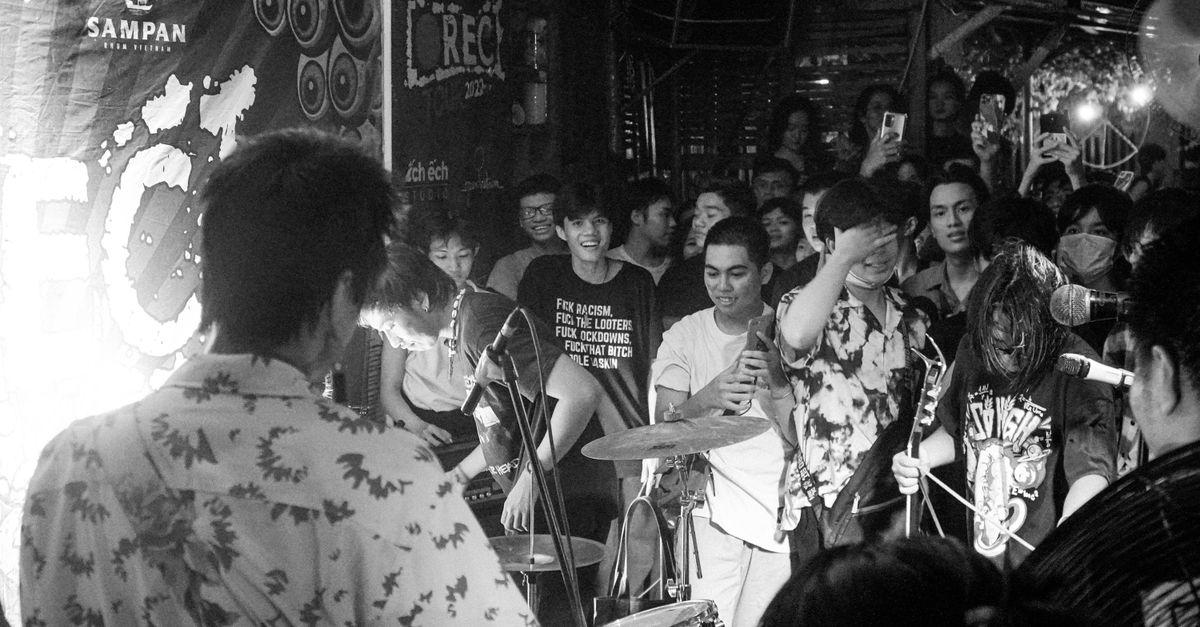 Black and white photo of a lively band performing to a crowd at an indoor venue.