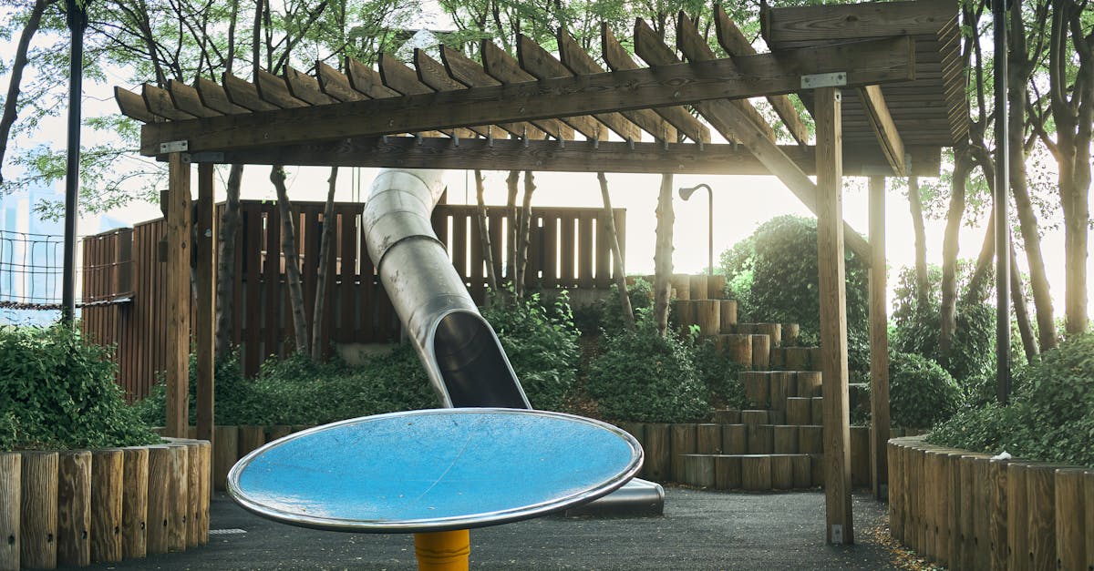 An urban playground featuring a slide and wooden pergola surrounded by trees and greenery.