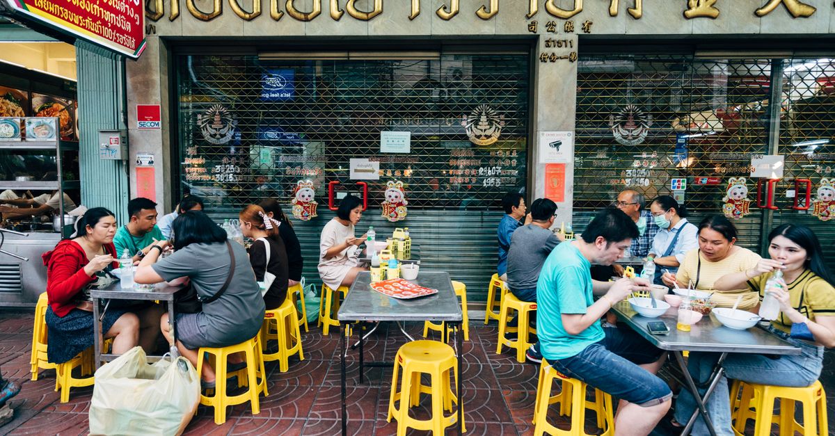 People enjoying authentic Thai street food at outdoor tables in Bangkok city.