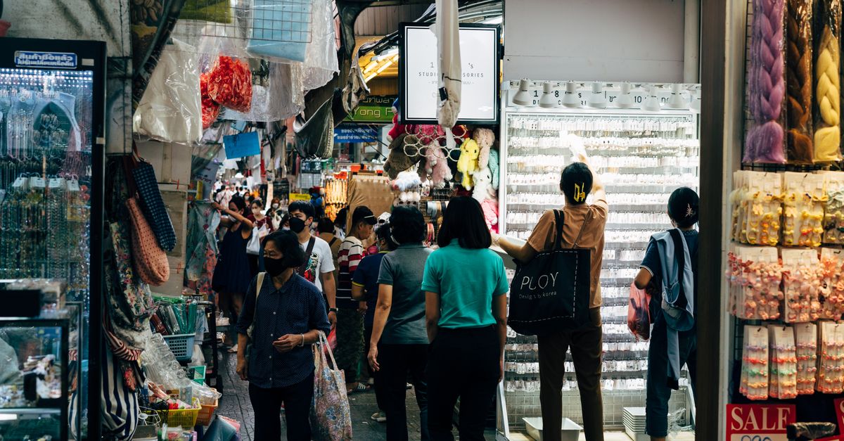 A busy marketplace filled with people shopping among colorful stalls and various goods.
