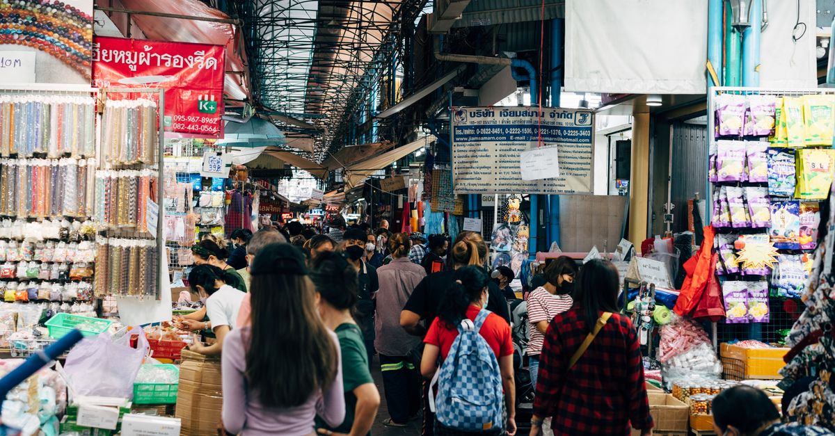 A crowded market in Bangkok with people shopping at various stalls, showcasing vibrant local culture.