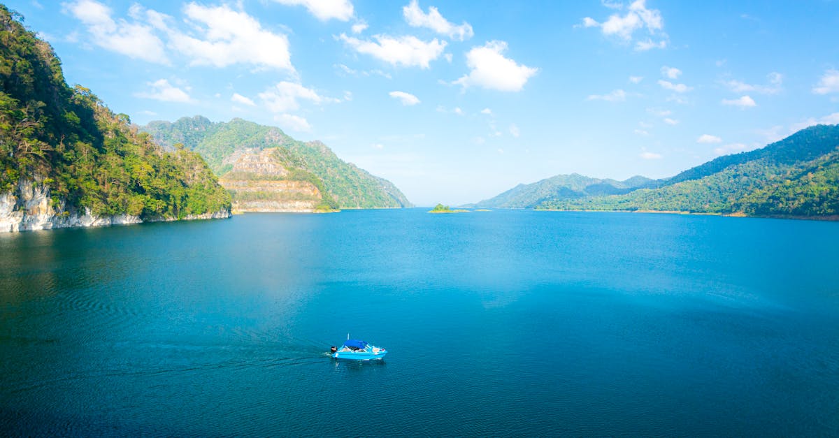 A tranquil view of a blue lake surrounded by lush green hills under a clear sky in Thailand.