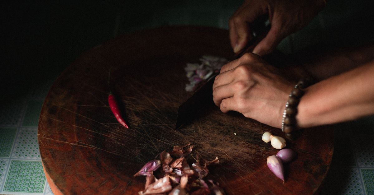 Close-up of hands chopping vegetables on a wooden cutting board in a kitchen setting.