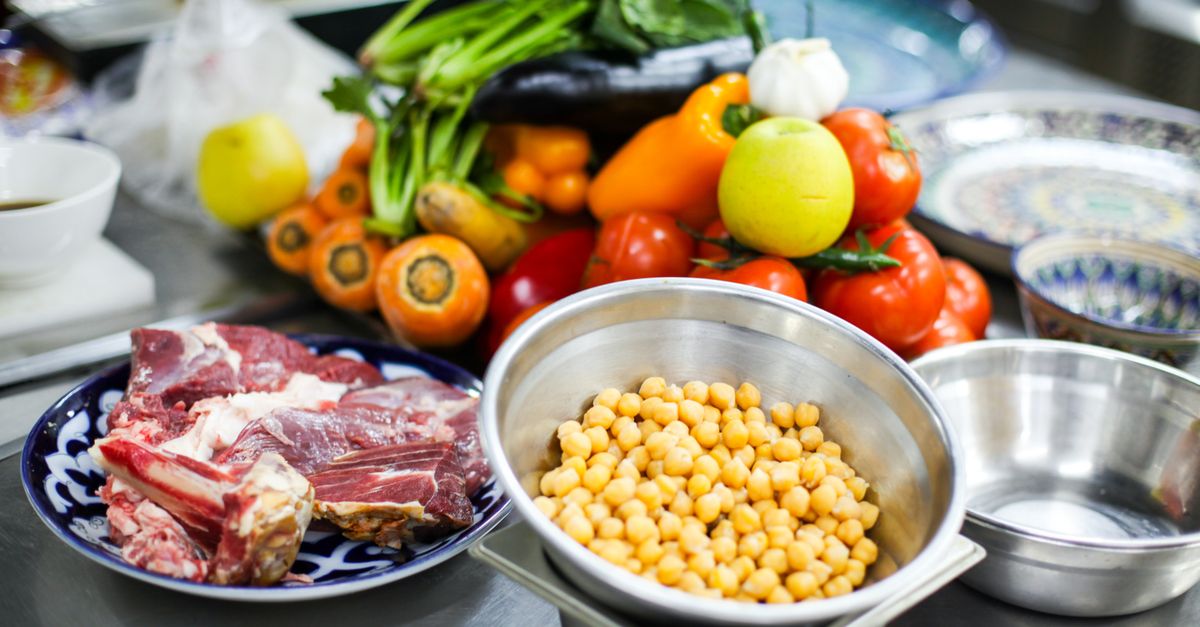Chickpeas, fresh vegetables, and raw meat on plates in a kitchen.