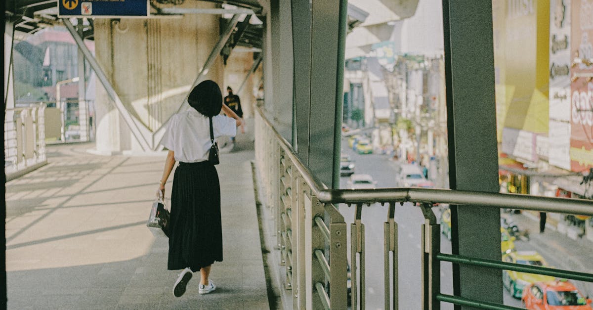 A woman walks on a city bridge pathway in Bangkok, Thailand, with urban scenery visible.