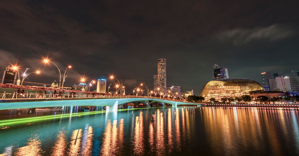 Stunning night view of Singapore skyline with illuminated bridge and reflections on water.