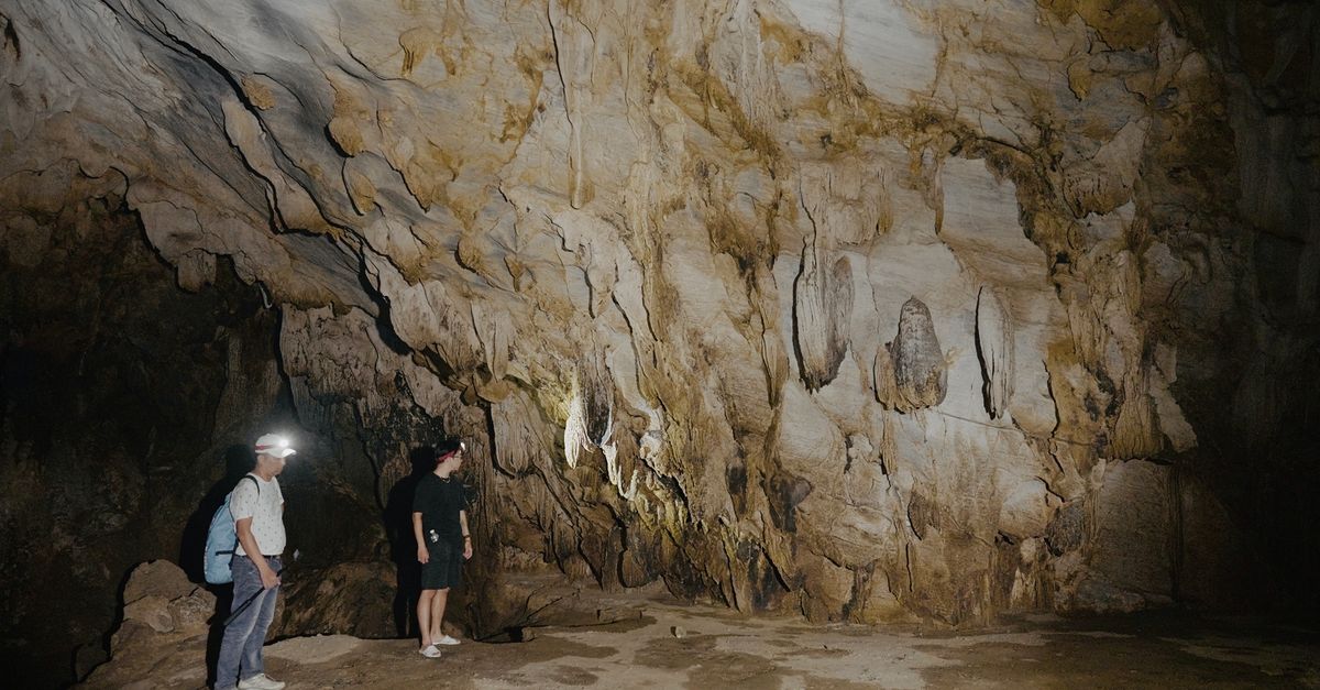 Two people exploring a vast limestone cave, illuminated by flashlights.