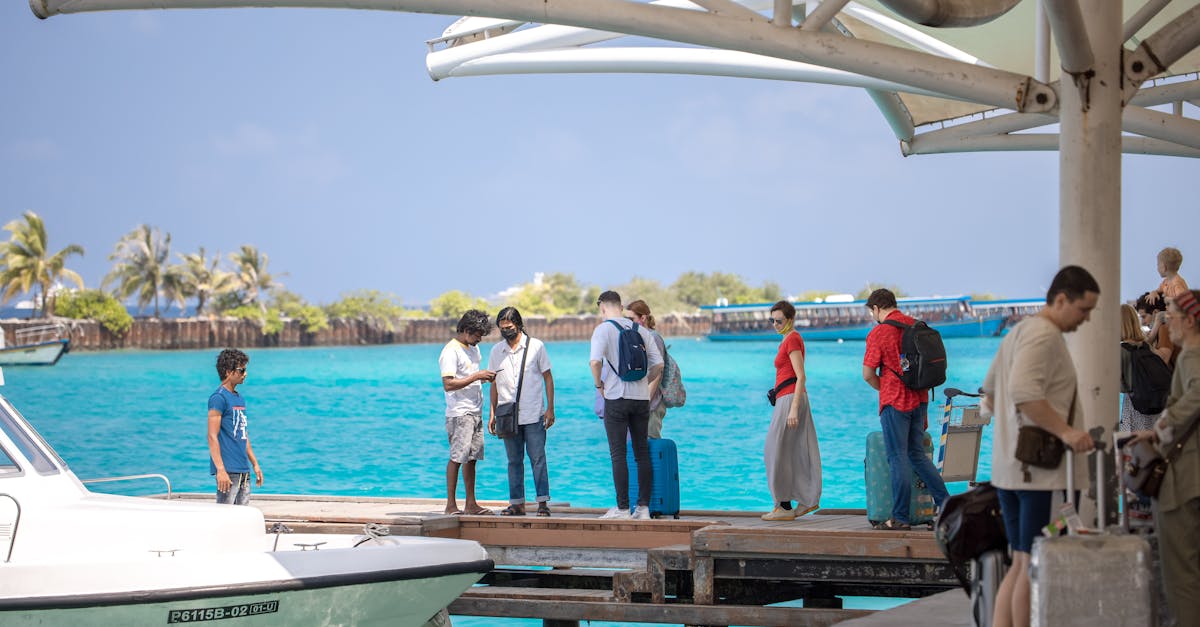 People with luggage waiting on a dock with turquoise ocean and clear sky in a tropical setting.