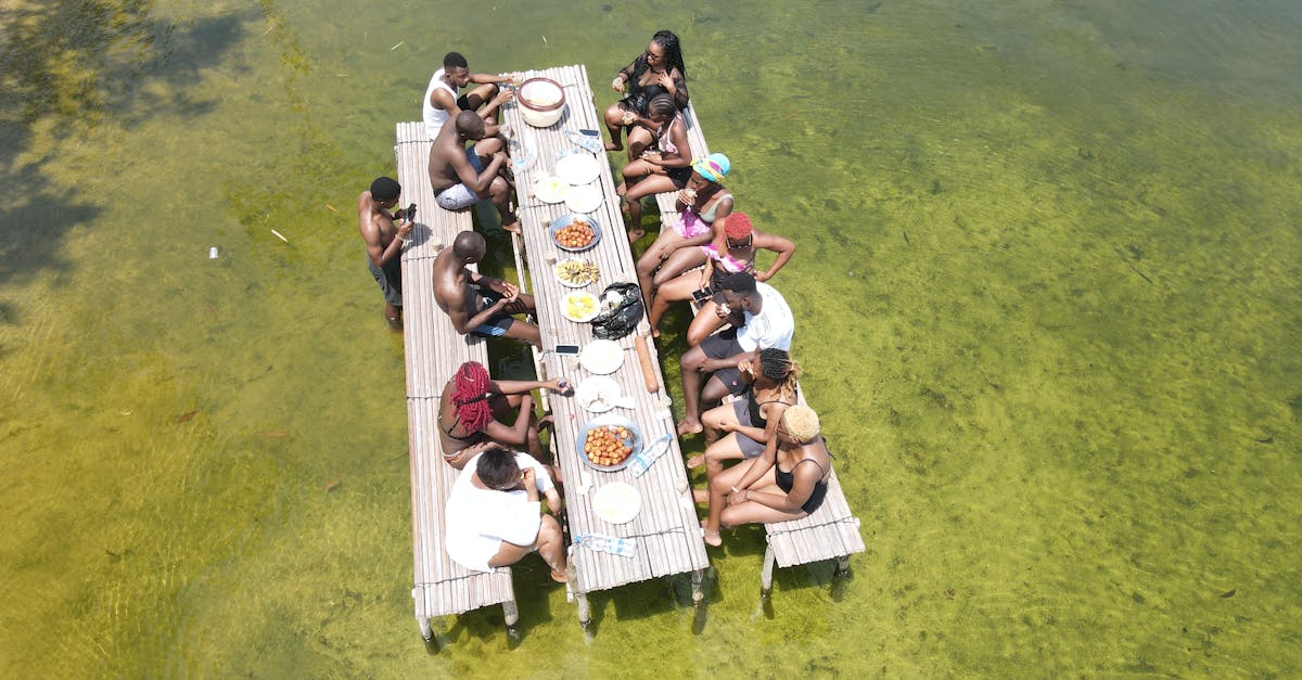 A group of friends enjoying a meal on a floating deck over a calm, clear water setting, viewed from above.