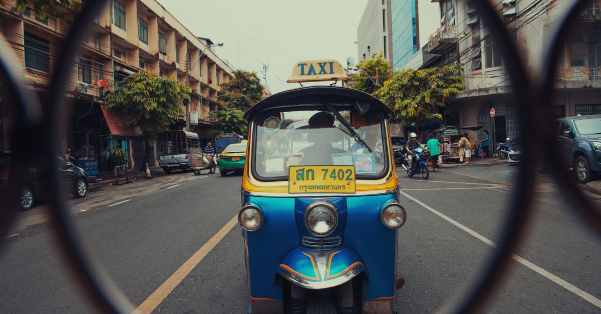 A colorful tuk-tuk on a busy urban street surrounded by city life and architecture.