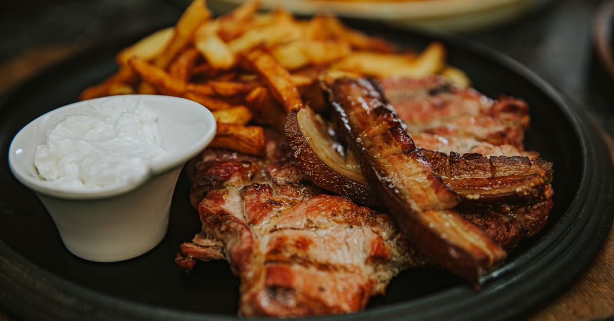 Savory grilled meat served with crispy fries and creamy sauce on a dark plate.