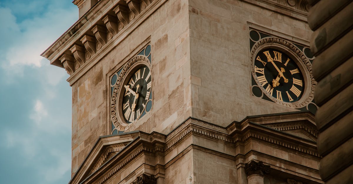 Low angle shot of a historic clock tower with Roman numerals, showcasing architectural details against a cloudy sky.