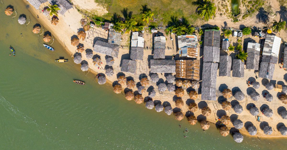 Stunning aerial view of a tropical beach resort in Conde, Brazil, with umbrellas and boats along the coastline.