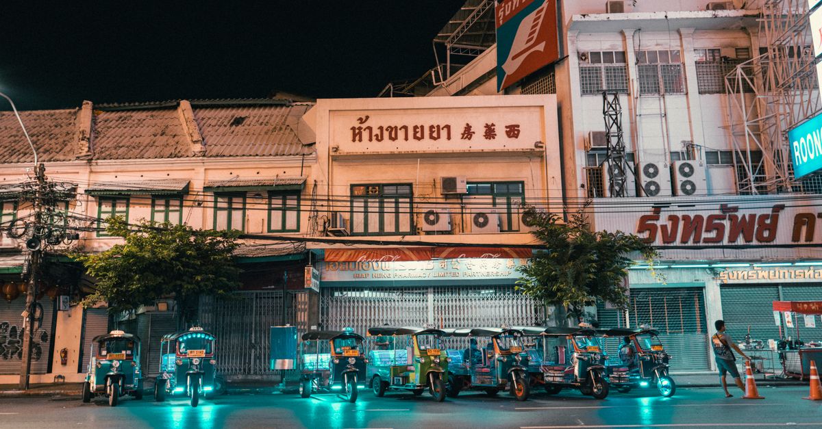 Vibrant night scene featuring electric tuk-tuks parked in front of lit-up city buildings.