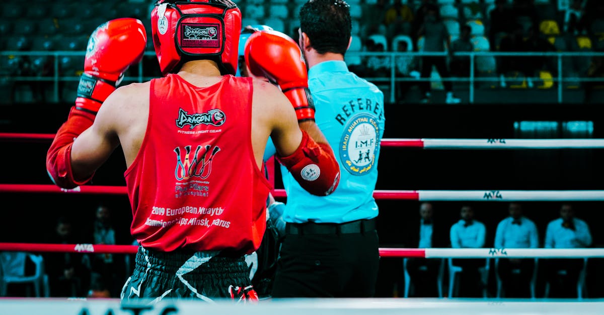 Rear view of a Muay Thai boxer in red gear facing the referee inside a boxing ring.