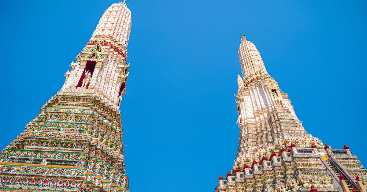 Low angle view of Wat Arun's ornate towers against a clear blue sky in Bangkok, Thailand.