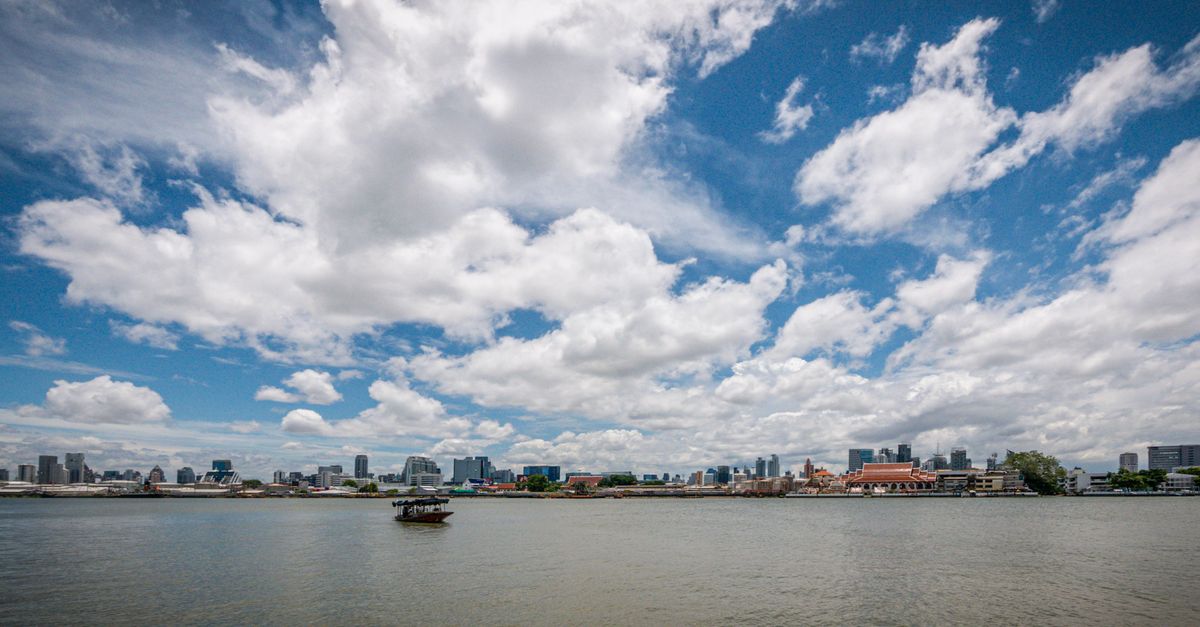 Panoramic view of Bangkok's skyline across the Chao Phraya River with cloudy skies, showcasing urban waterfront charm.