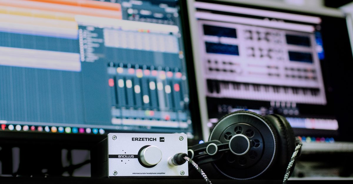 Close-up of a professional music studio setup featuring an amplifier and headphones with digital audio workstations in the background.