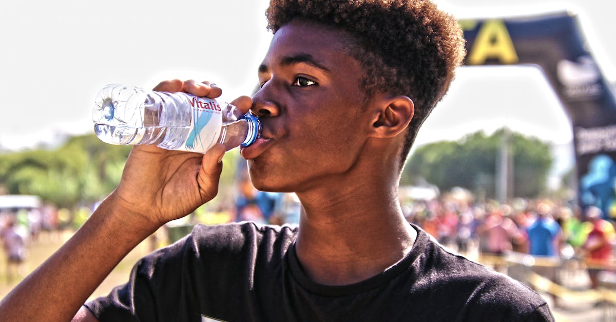 A young man drinking bottled water outdoors at a sporting event, showcasing hydration and fitness.