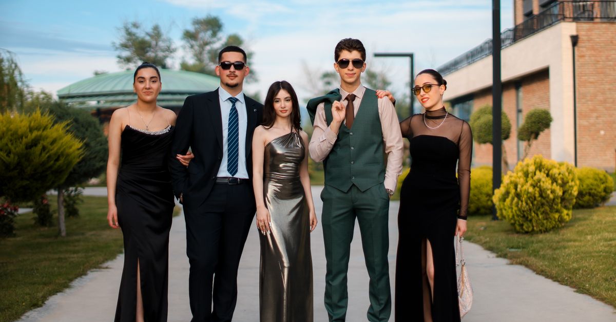 A stylish group of five adults in formal attire posing outdoors on a sunny day.