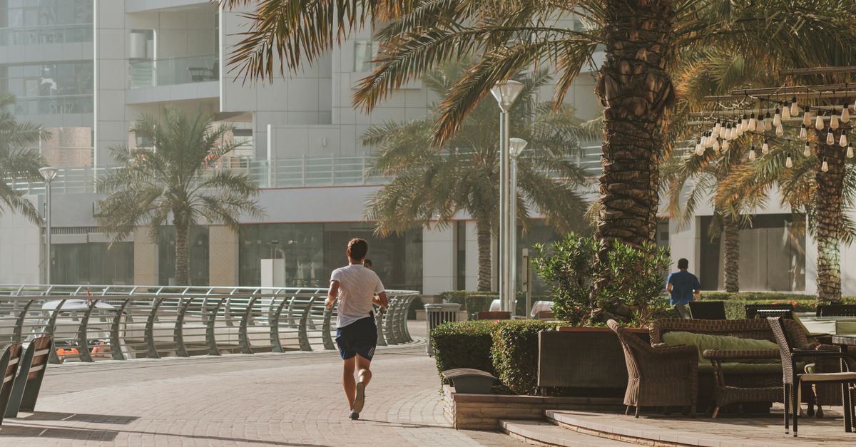 A jogger enjoying a morning run along the scenic Dubai Marina promenade, surrounded by palm trees and luxury buildings.