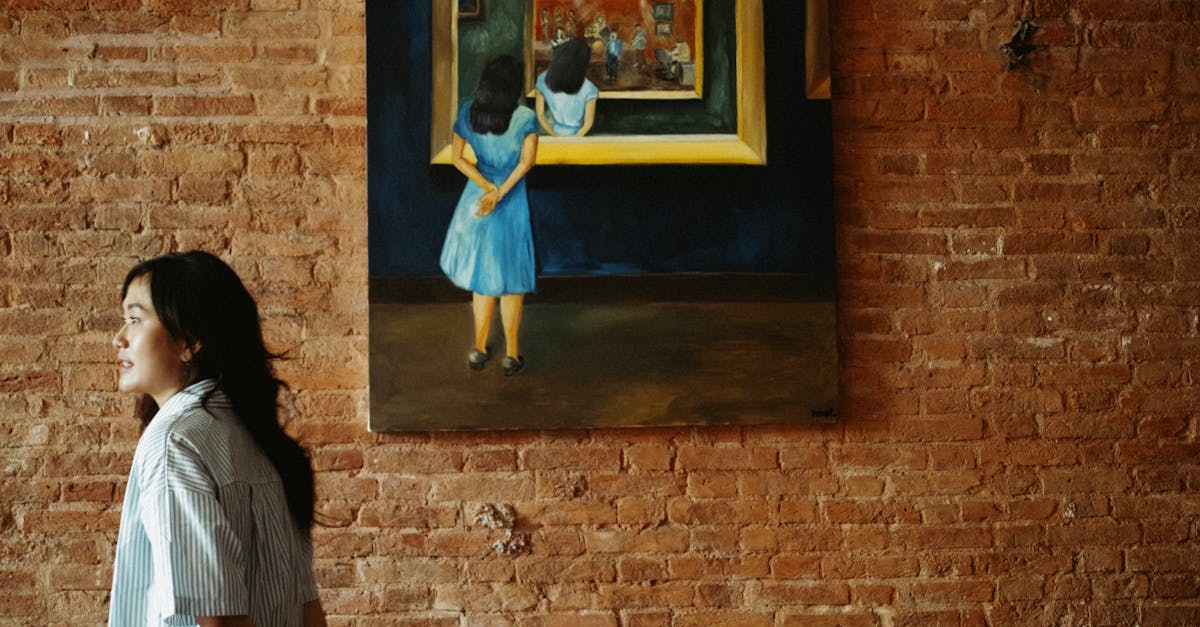 Woman stands by a painting on a brick wall, exploring art in a casual setting.