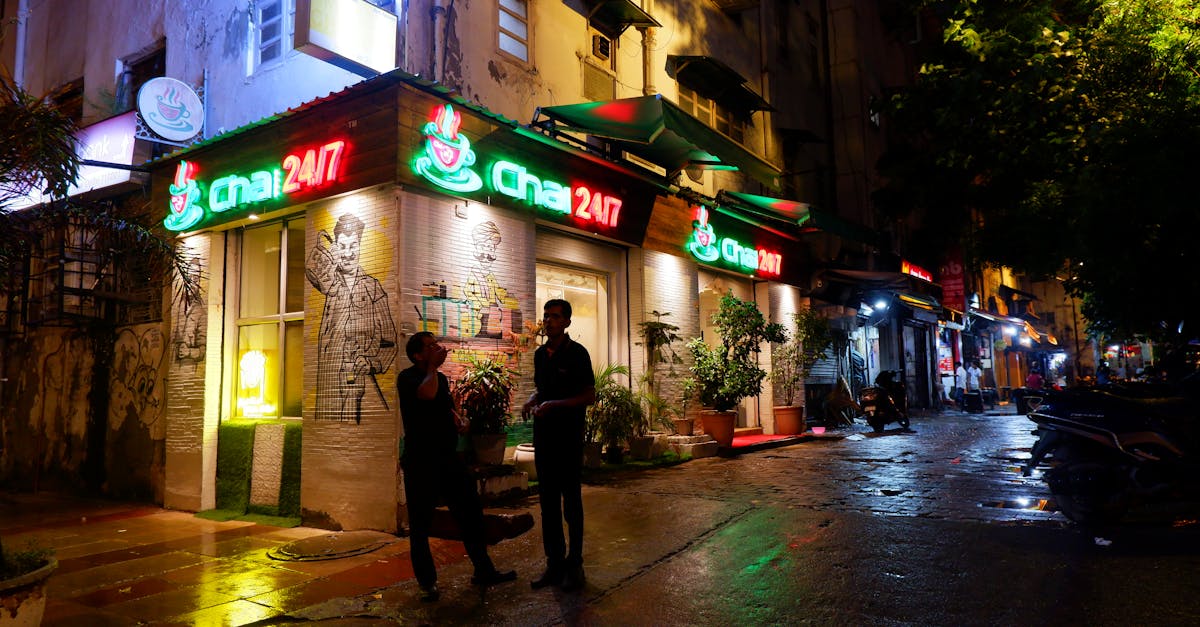 A vibrant street scene at night featuring a glowing cafe storefront and two adults conversing.