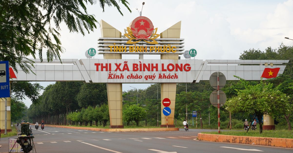 View of the entrance archway to Bình Long in Bình Phước Province, Vietnam with motorbikes passing by.
