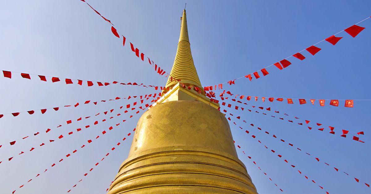Striking view of a golden chedi adorned with red flags against a clear Bangkok sky.