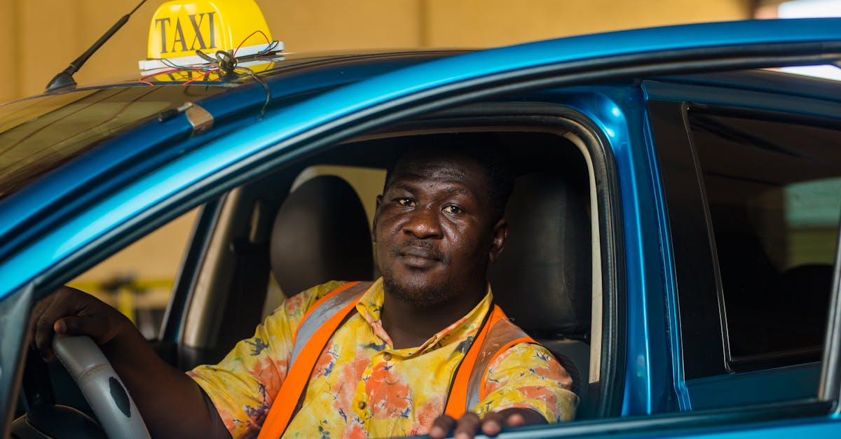 A Ghanaian taxi driver in a colorful shirt sits inside his blue vehicle, ready for passengers.