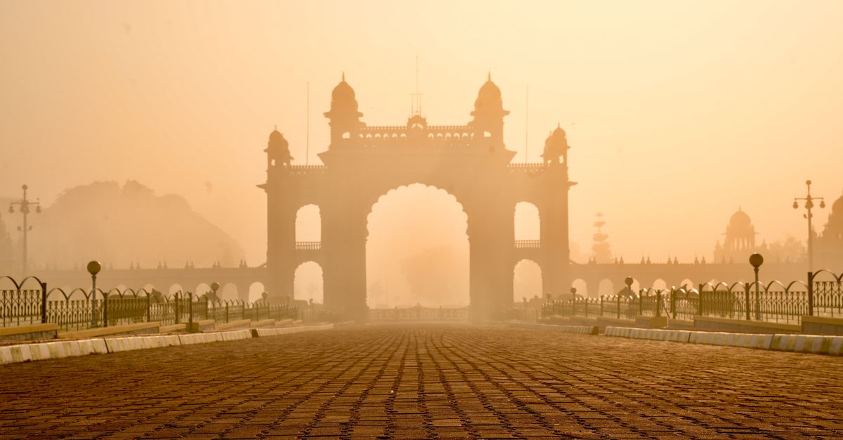The Mysore Palace gate stands majestically enveloped in a golden morning fog, showcasing elegant 18th-century architecture.