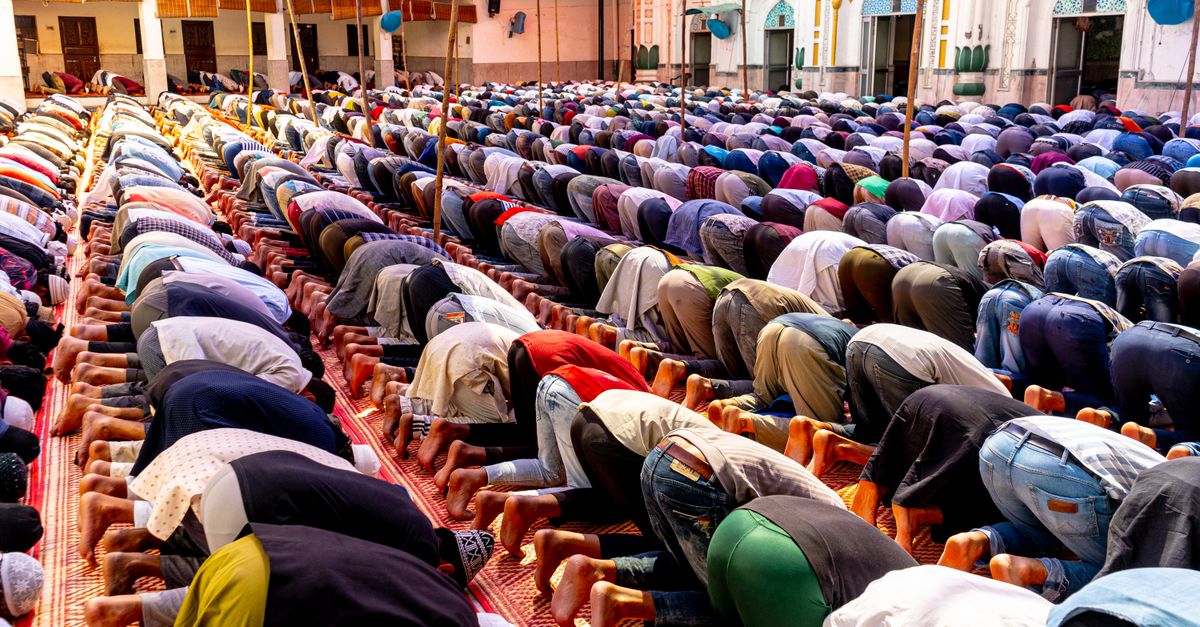 A gathering of people in prayer at an outdoor mosque courtyard during daytime.