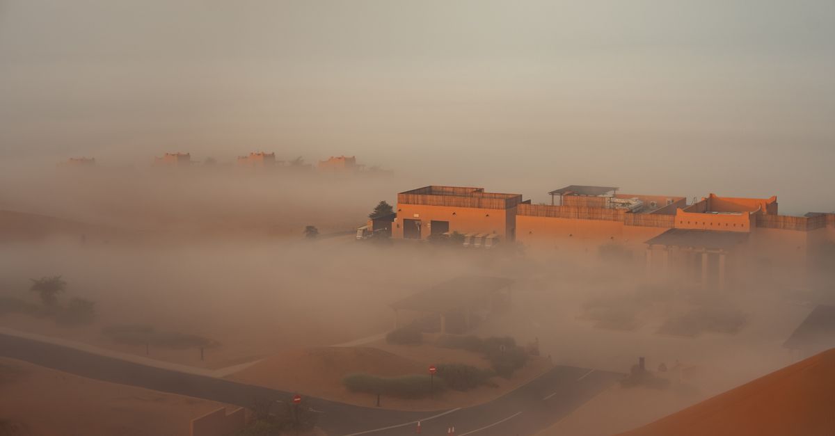Aerial view of desert buildings enveloped in morning fog, casting a serene and mysterious ambiance.