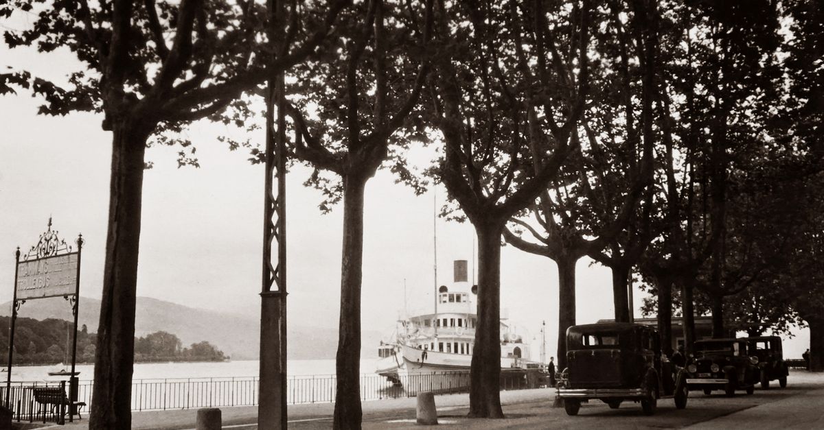 Scenic vintage riverside with parked classic cars and a docked boat.