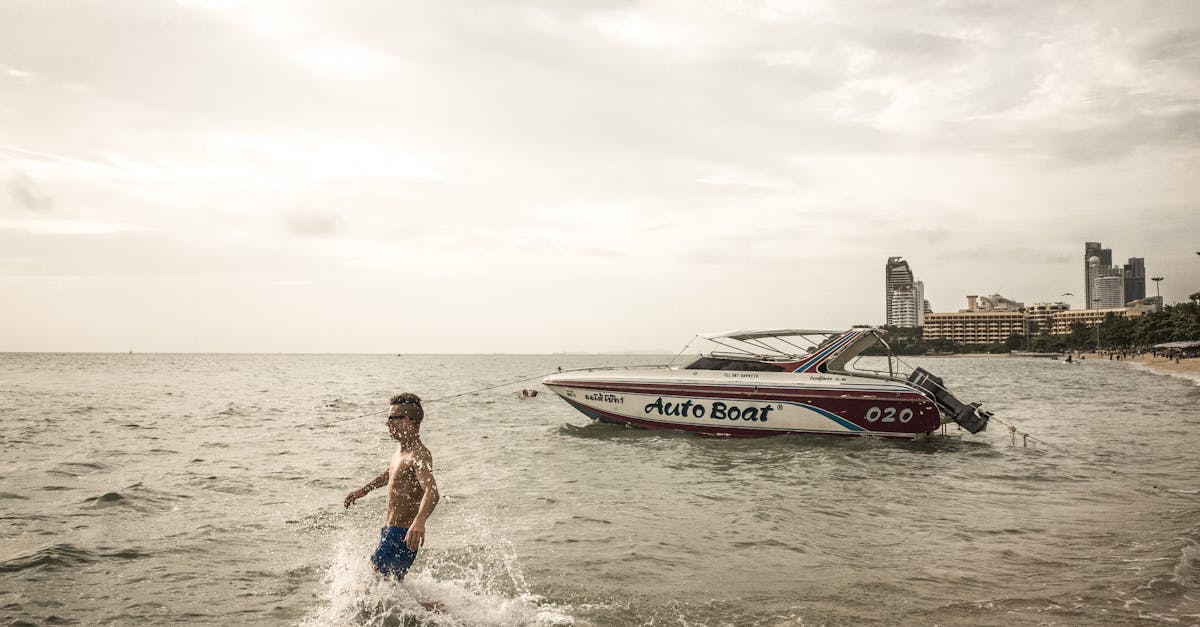 A young boy plays in the sea with a speedboat and city skyline in the background.
