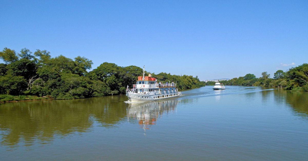 A serene river with two boats sailing surrounded by lush greenery and clear blue sky.