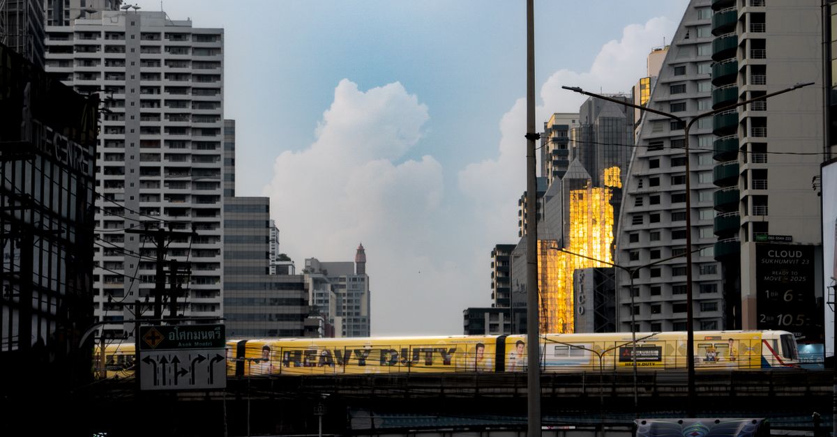 Cityscape featuring Bangkok's skytrain with golden reflections on skyscrapers at sunset.