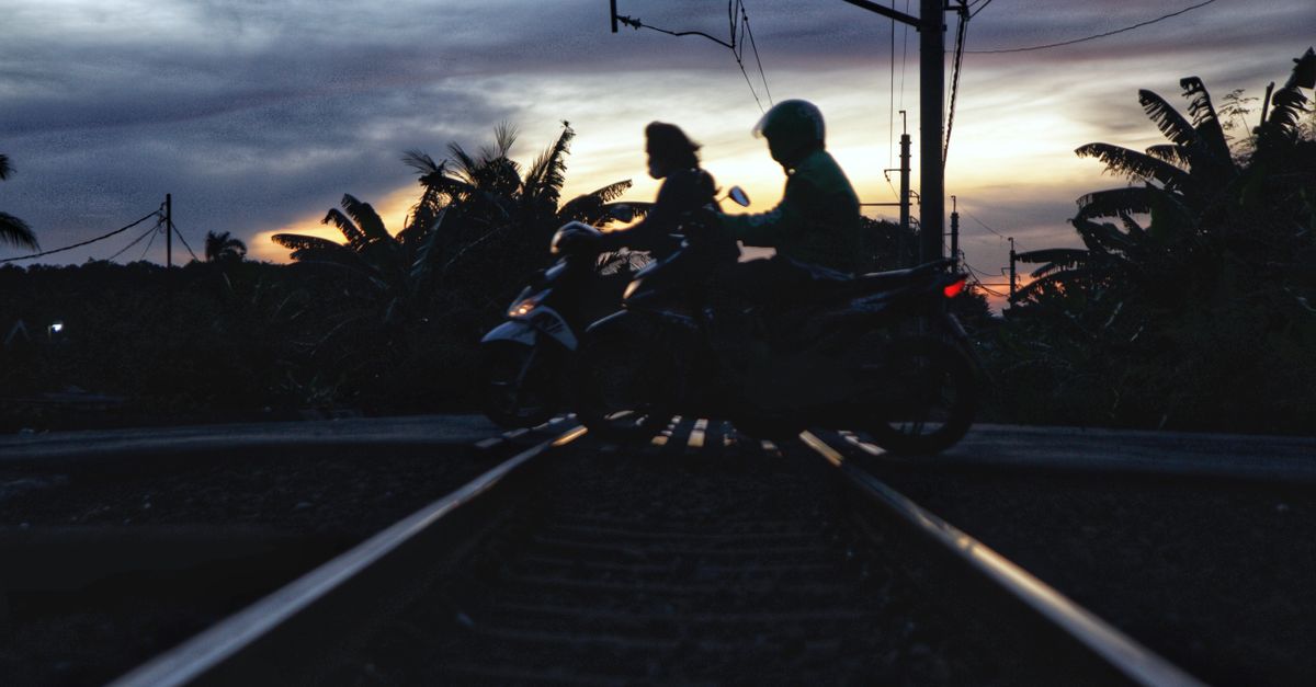 A motorbike crosses a railway track at twilight, silhouetted against a vivid sunset sky.