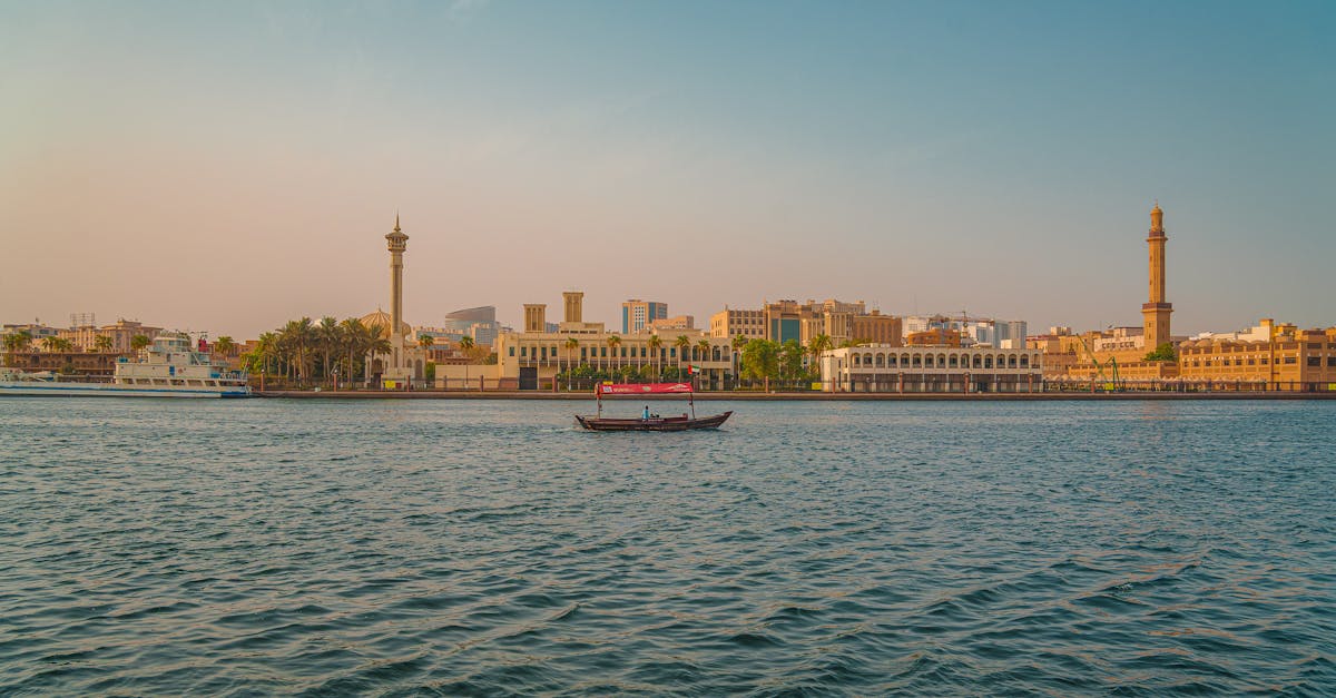 Scenic sunset view of Dubai Creek featuring traditional boats and a skyline of iconic Middle Eastern architecture.